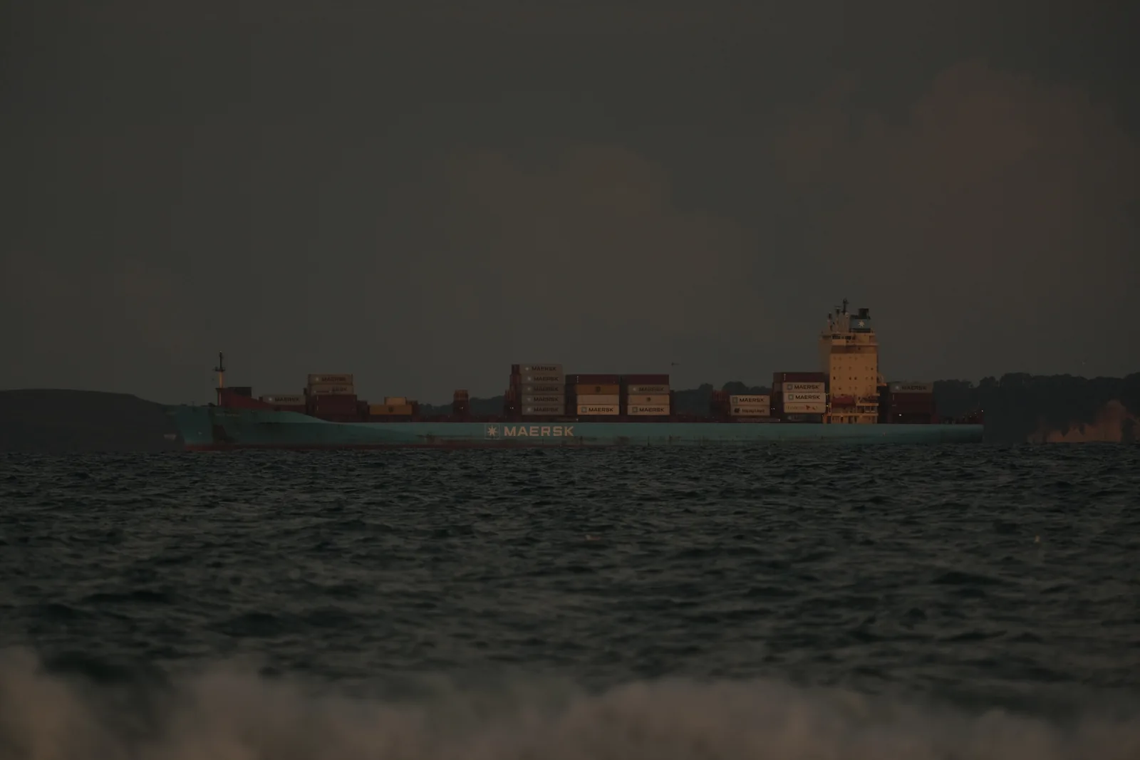 A Maersk container ship on dark water at dusk